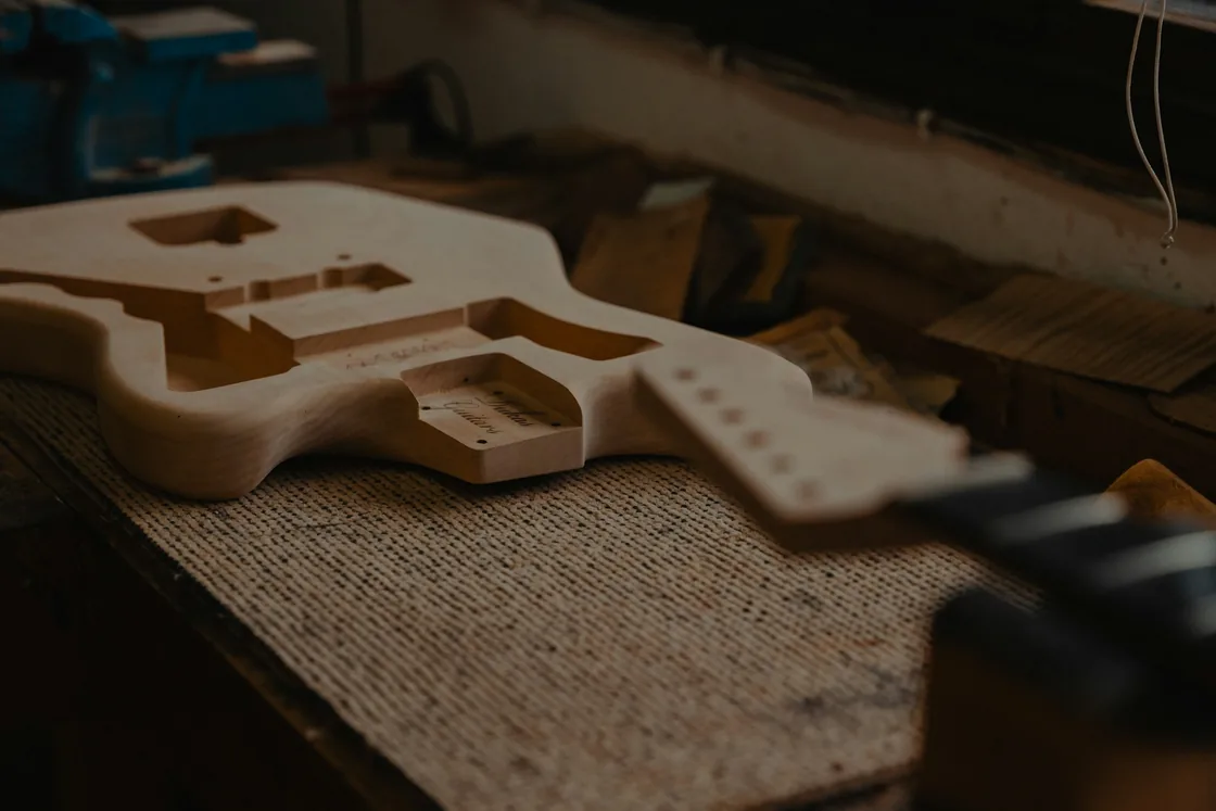 Cuerpo de guitarra sin acabar y mástil en bruto apoyados sobre el banco de un taller de lutería